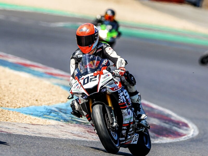 Pilote en tenue noire et blanche sur une moto blanche, prenant un virage serré sur un circuit de course.