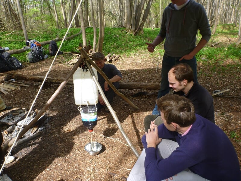 Trois personnes en forêt observant un système de filtration d'eau suspendu entre des branches d'arbres.