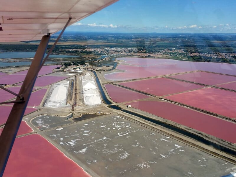 Salins aux bassins roses et blancs vus depuis les airs, avec une ville en arrière-plan sous un ciel clair