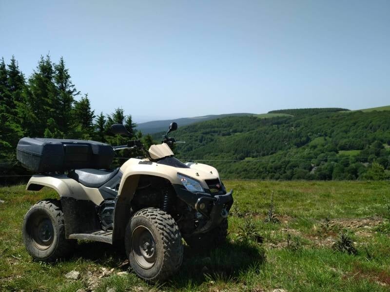 Quad beige garé sur une prairie avec une vue dégagée sur des collines verdoyantes au loin.