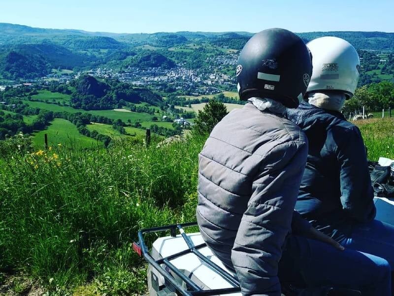 Deux personnes assises sur un quad regardant un paysage vallonné et verdoyant sous un ciel clair.