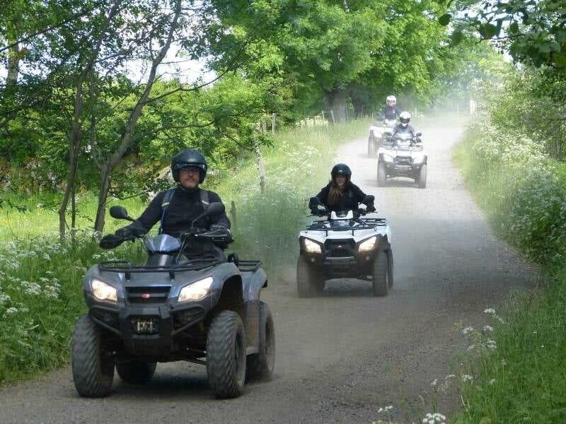 Groupe de trois personnes en quads roulant sur un chemin de terre entouré d'arbres verts.