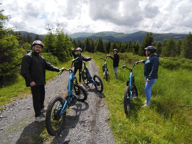 des randonneurs posent en trottinette sur un chemin rocailleux du Cantal