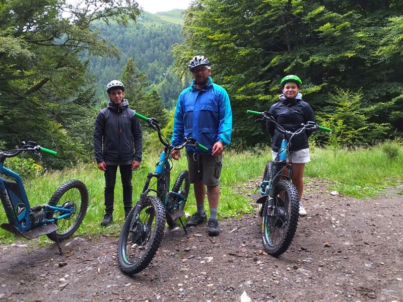 3 personnes font une pause durant leur balade en trottinette électrique au bord d'un chemin de forêt