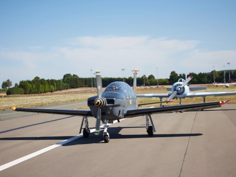 Petit avion de voltige gris avec hélice en mouvement sur piste d'aéroport par temps clair et ciel bleu