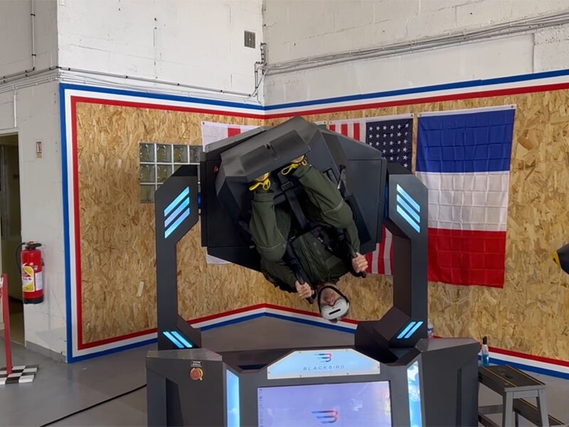 Personne utilisant un simulateur de vol gyroscopique, suspendue à l'envers en position de vol inversé, portant un casque VR.