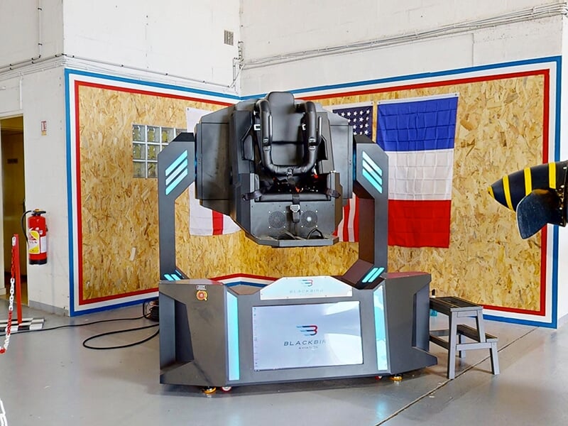Simulateur de vol gyroscopique à l’arrêt, sans occupant, avec drapeaux américain et français en arrière-plan