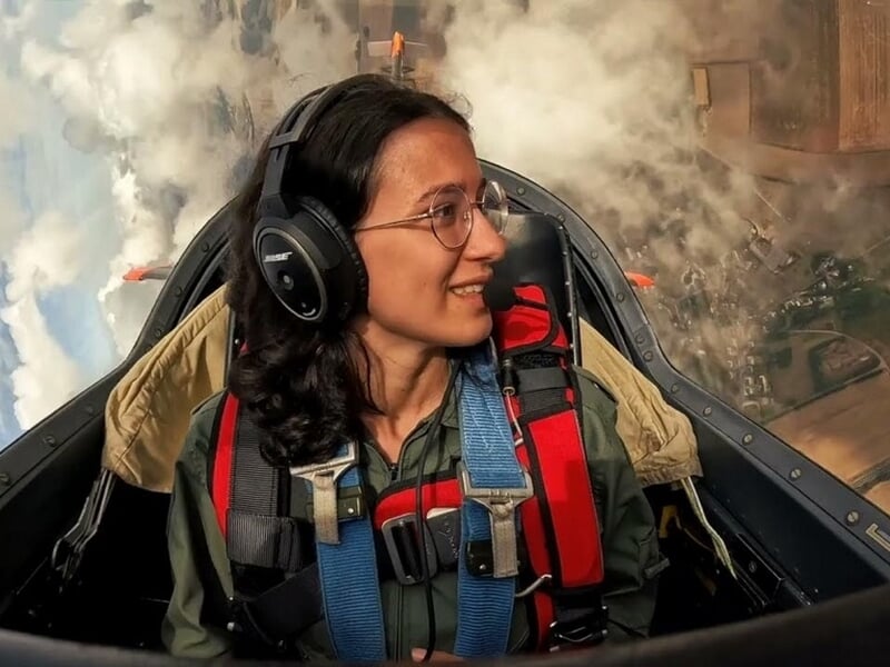 Femme souriante avec casque et lunettes dans le cockpit d'un avion en vol,lors d'un vol en avion Stampe à Cergy.