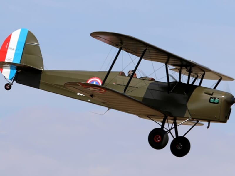 Avion biplan militaire vert en vol avec un pilote visible dans le cockpit, lors d'un vol en avion Stampe à Cergy.