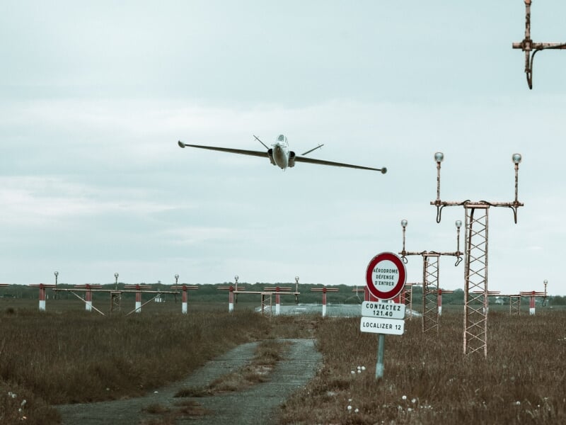 Jet militaire en approche de la piste d'atterrissage, survolant des balises lumineuses avec un panneau d'interdiction d'entrée en premier plan.