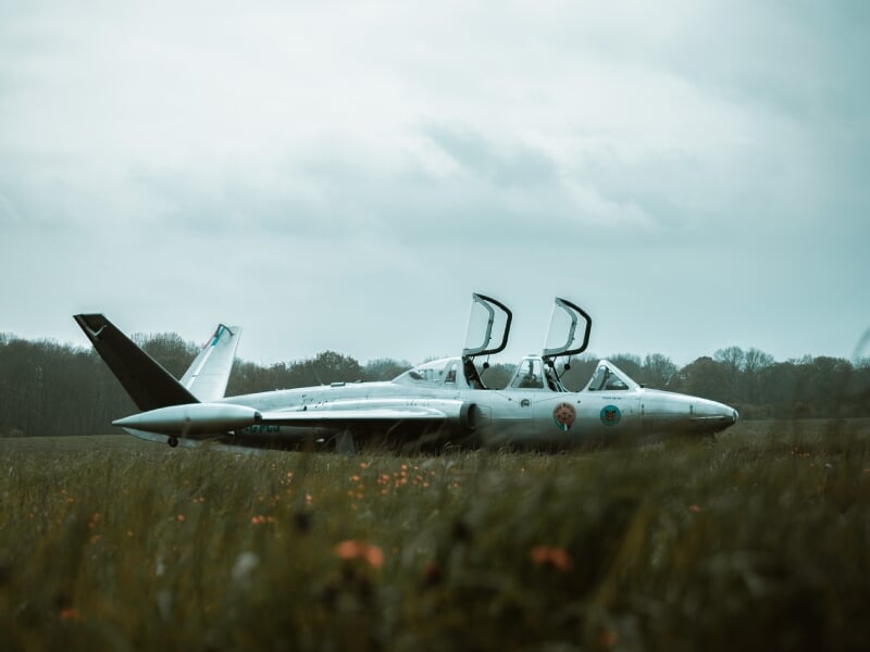 Deux Alpha Jet stationnés dans un champ, cockpit ouvert, dans un paysage nuageux et herbeux.
