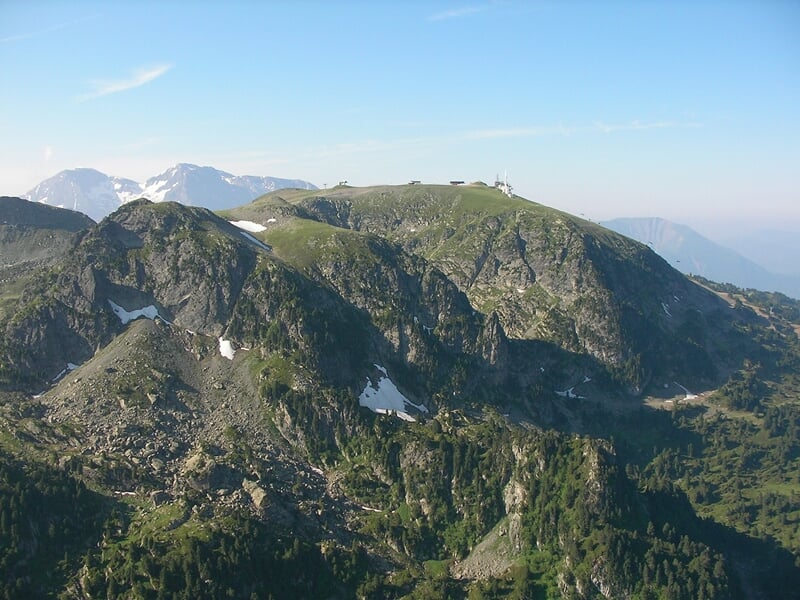 Montagne verdoyante avec quelques zones rocheuses et un ciel clair, prise depuis un point élevé.