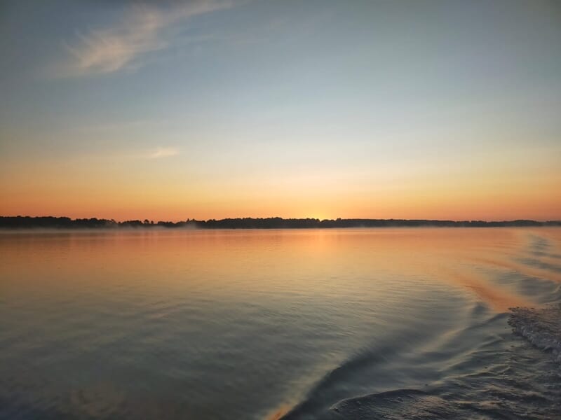 Coucher de soleil sur un lac calme avec des reflets orangés et une légère vague lors d'un séjour avec un guide de pêche sur les lacs des Landes.