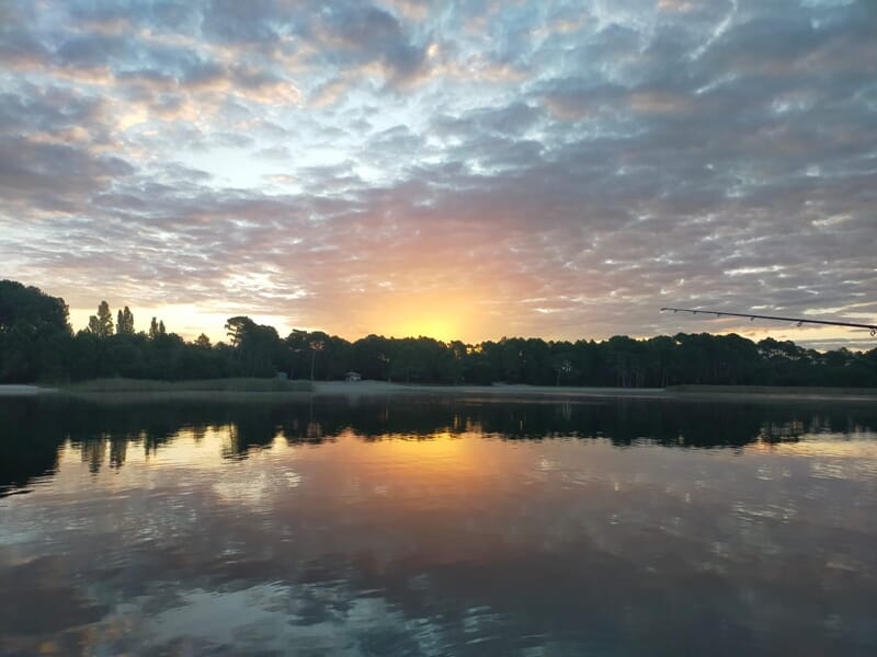 Paysage au crépuscule avec un ciel nuageux coloré et un lac reflétant les teintes du soleil couchant lors d'un séjour avec un guide de pêche sur les lacs des Landes.