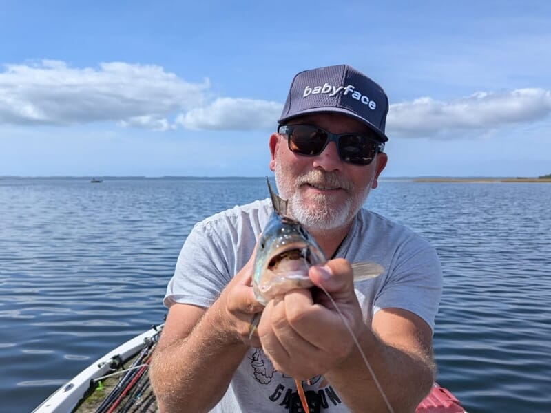 Homme souriant portant une casquette et des lunettes de soleil lors d'un séjour avec un guide de pêche sur les lacs des Landes.