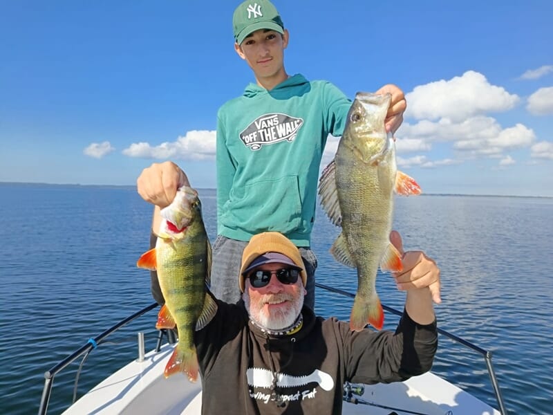 Deux pêcheurs sur un bateau tenant chacun une grosse perche lors d'un séjour avec un guide de pêche sur les lacs des Landes.
