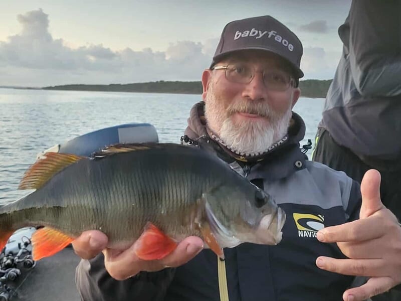 Homme avec casquette et lunettes tenant un poisson coloré lors d'un séjour avec un guide de pêche sur les lacs des Landes.