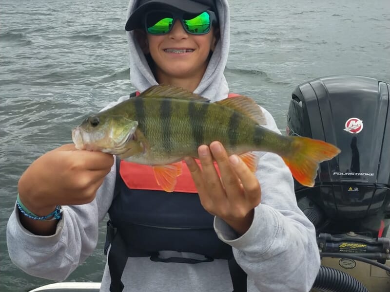 Jeune pêcheur souriant tenant un poisson coloré lors d'un stage de pêche pour enfant sur les lacs des Landes.