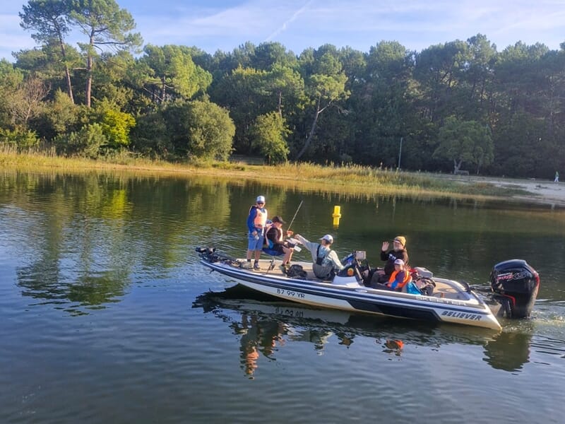 Quatre personnes sur un bateau de pêche naviguant lors d'un stage de pêche pour enfant sur les lacs des Landes.