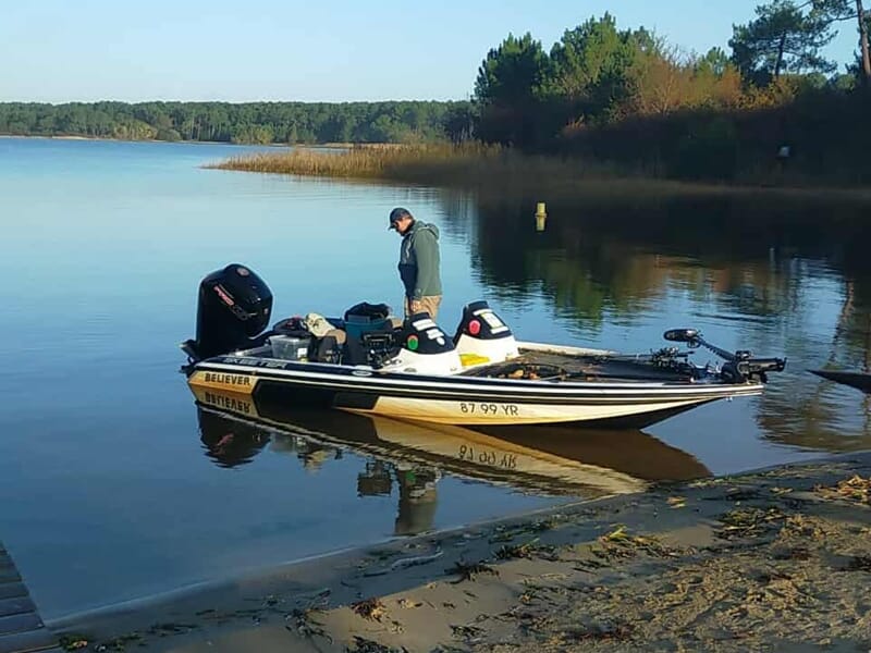 Bateau de pêche amarré au bord d'un lac paisible avec un pêcheur debout sur la rive lors d'un stage de pêche pour enfant sur les lacs des Landes.