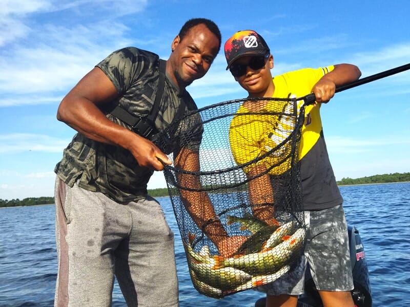 Deux hommes debout sur un bateau, tenant une grande épuisette remplie de poissons fraîchement pêchés.