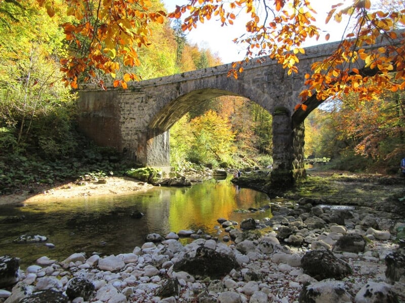 Pont en pierre au-dessus d'une rivière entourée d'arbres aux feuilles d'automne colorées