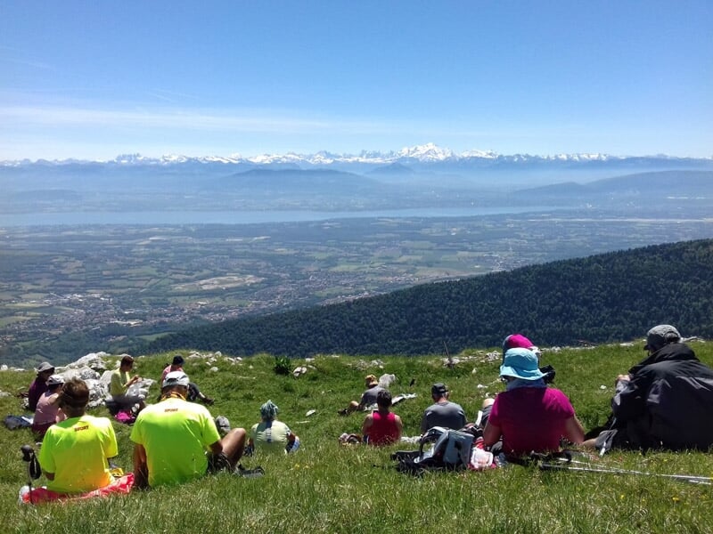 Groupe de randonneurs assis sur une colline verte avec vue sur une vallée et des montagnes au loin