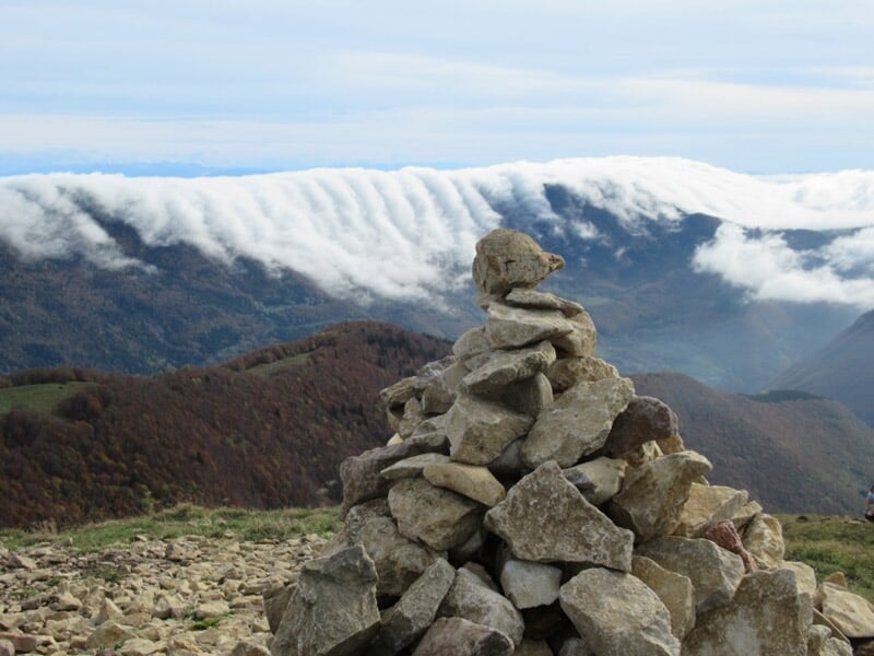 Tas de pierres empilées sur un sommet avec un paysage de montagnes et un ciel nuageux en arrière-plan