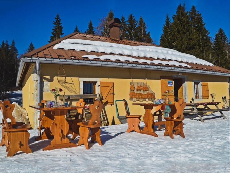 Chalet en bois jaune avec mobilier extérieur en bois sur un sol enneigé entouré d'arbres verts