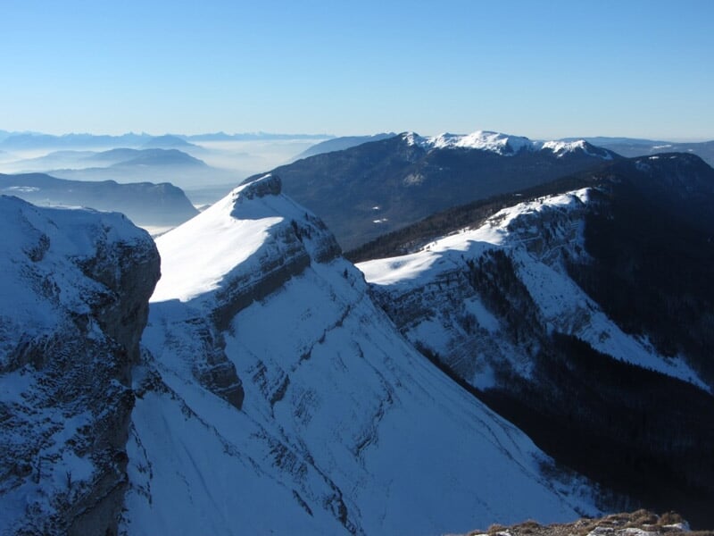 Paysage de montagne enneigée avec arbres recouverts de neige et ciel bleu avec nuages légers