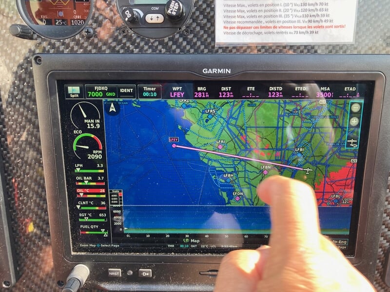 Écran de navigation Garmin dans un cockpit d'avion montrant une carte de vol avec une main pointant l'écran.