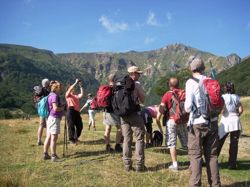 Randonneurs avec sacs à dos et bâtons, admirant un panorama montagneux sous un ciel dégagé.