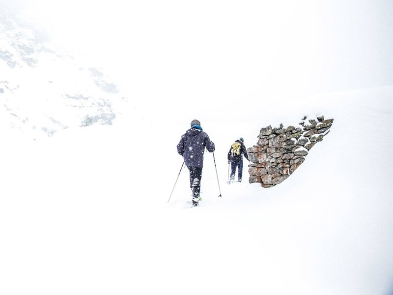Deux randonneurs en raquettes à neige progressant dans un paysage blanc et lumineux.