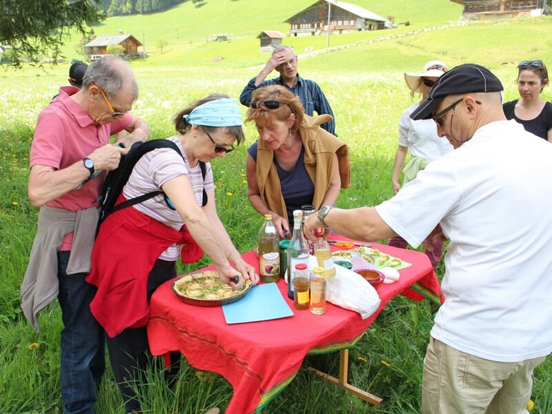 Groupe de randonneurs préparant un repas sur une table rouge en pleine nature verdoyante en France.