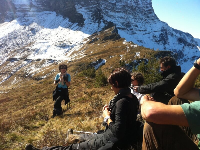 Randonneurs assis sur un sentier de montagne avec des sommets enneigés en arrière-plan.