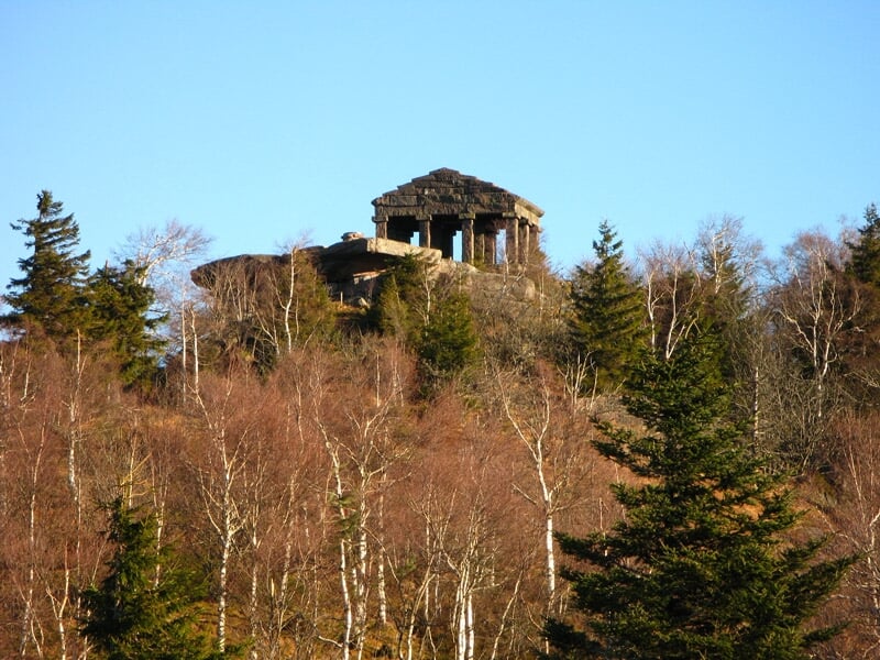 Temple ou monument en pierre sur une colline entourée d'arbres en automne