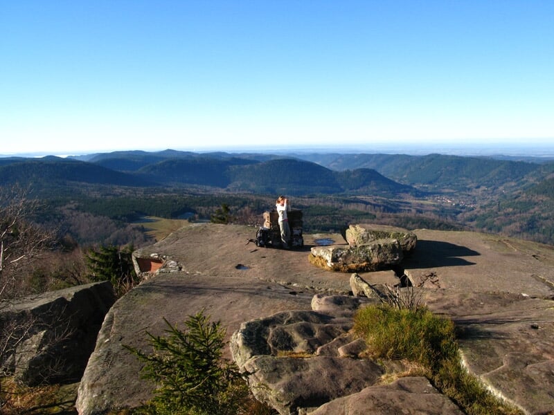 Vue depuis un sommet rocheux avec deux personnes assises et paysage vallonné à l'horizon