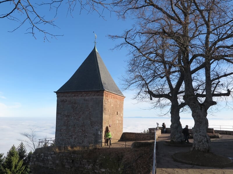 Tour carrée en pierre sur une colline avec une personne debout à côté et arbres