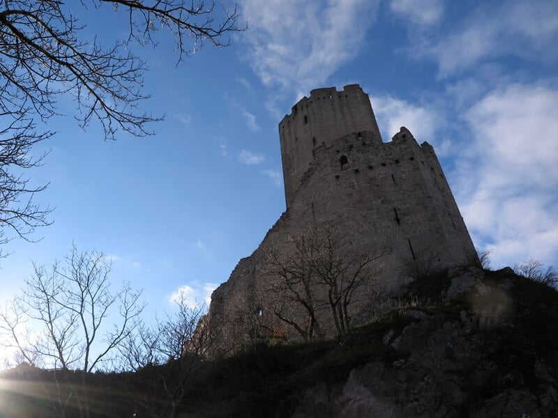 Château fort en pierre sur une colline avec arbres et ciel bleu partiellement nuageux