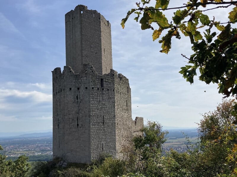 Château médiéval en pierre avec tour principale sous un ciel bleu avec quelques nuages