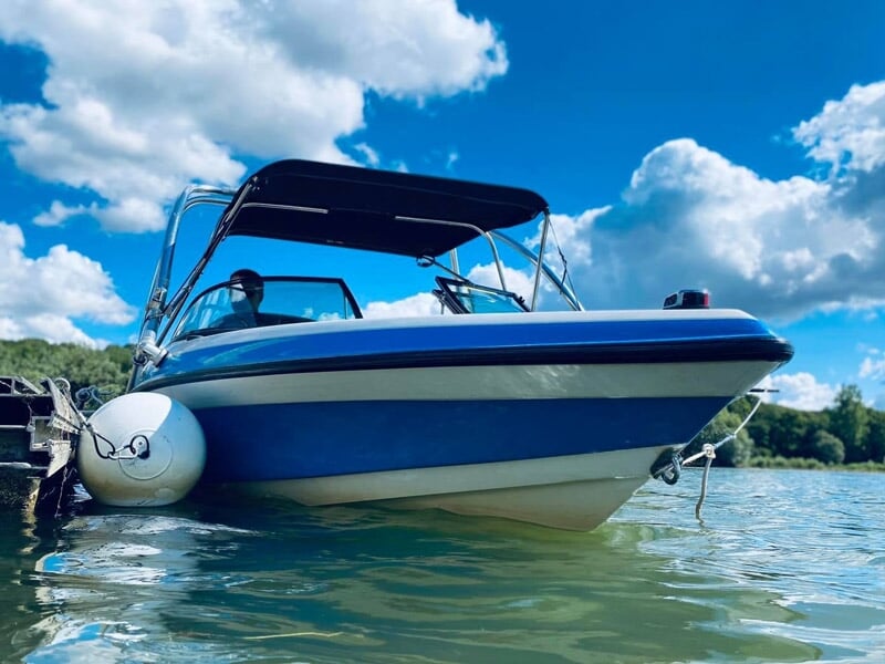 Bateau blanc et bleu amarré sur le lac de la Liez sous un ciel bleu avec quelques nuages blancs.
