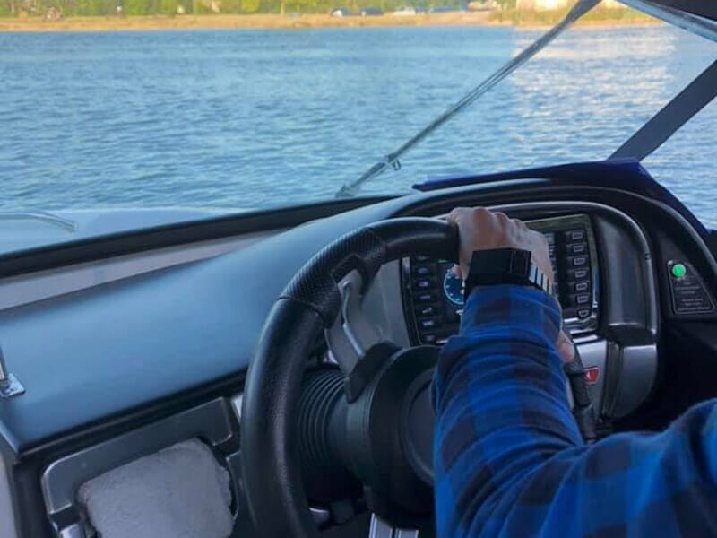 Vue rapprochée d'une main tenant le volant d'un bateau naviguant sur le lac de la Liez.