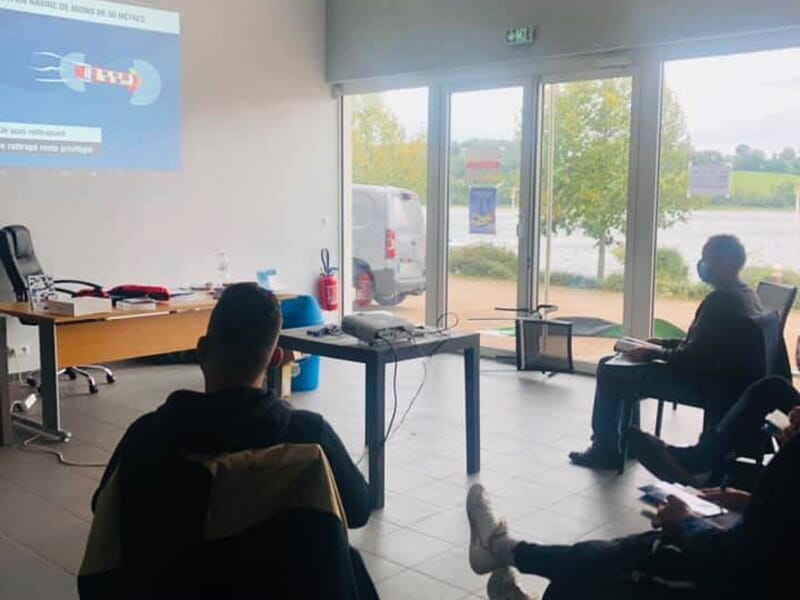 Personnes assises dans une salle lumineuse avec vue sur le lac, assistant à une formation ou réunion.