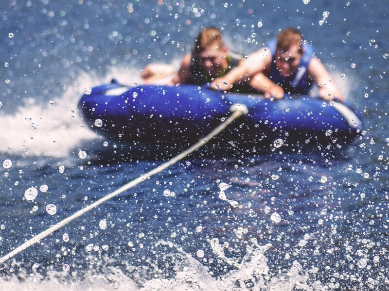 Deux enfants sur une bouée tractée par un bateau, éclaboussures d'eau autour sur le lac de la Liez.