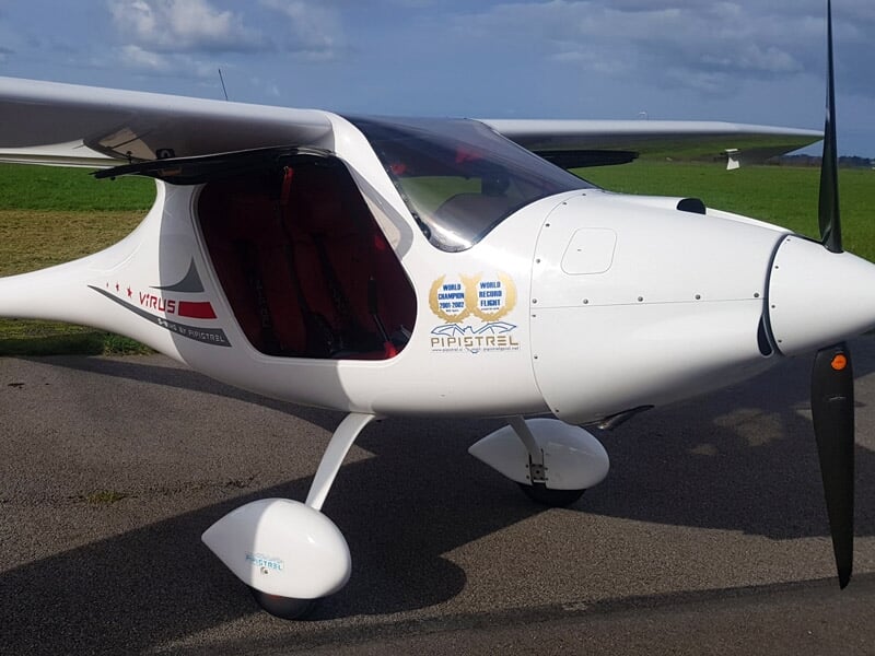 Avion léger blanc stationné sur une piste d'aérodrome avec ciel partiellement nuageux en arrière-plan.