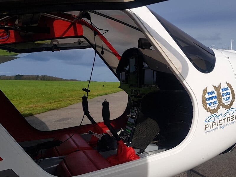 Intérieur d'un petit avion avec siège rouge et tableau de bord visible à travers la porte ouverte.