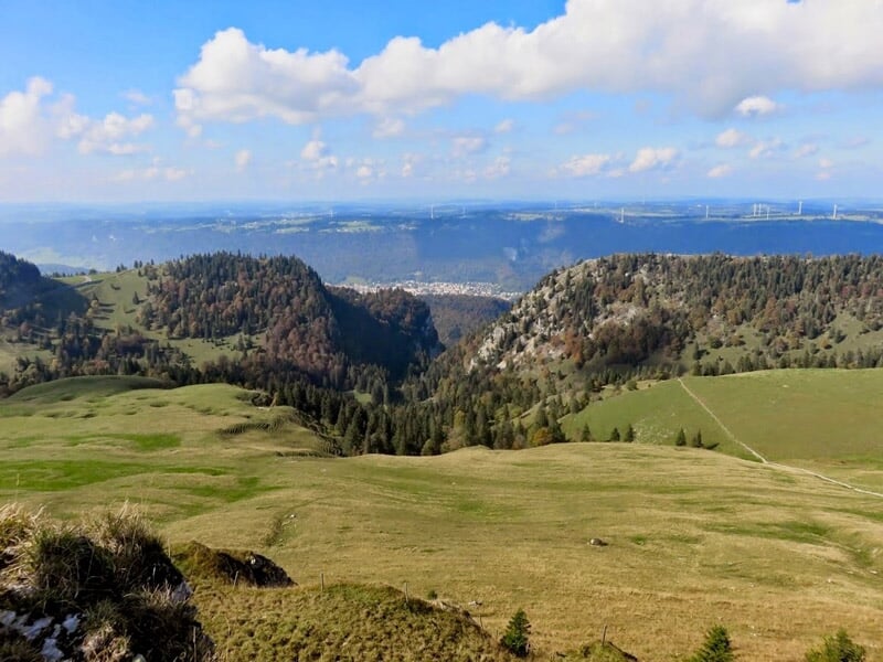 Vue panoramique d'une vallée verdoyante avec des collines et un ciel bleu clair.