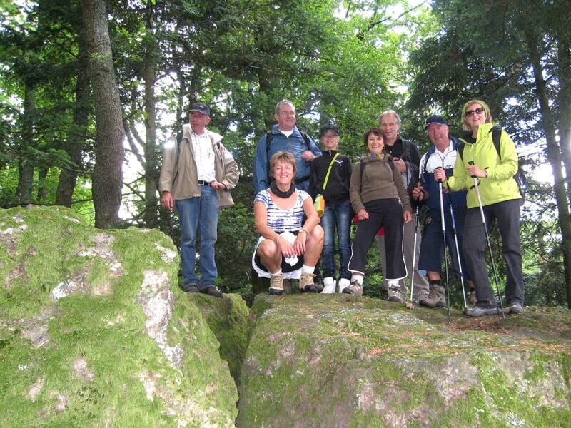 Groupe de randonneurs posant sur des rochers dans une forêt verdoyante.