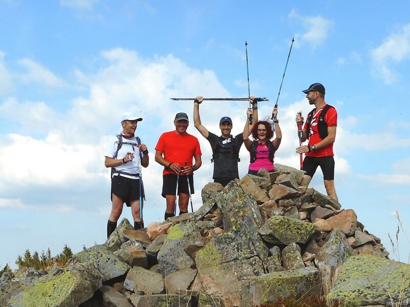 Cinq coureurs en tenue sportive posant au sommet d'une montagne rocheuse sous un ciel bleu.