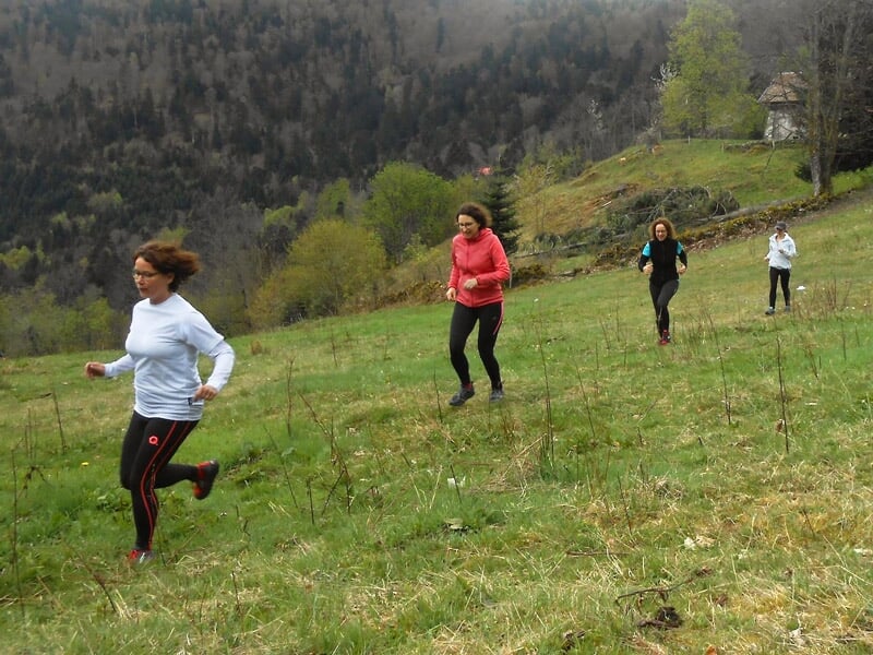 Quatre femmes courant dans un champ herbeux avec des arbres au loin sous un ciel nuageux.